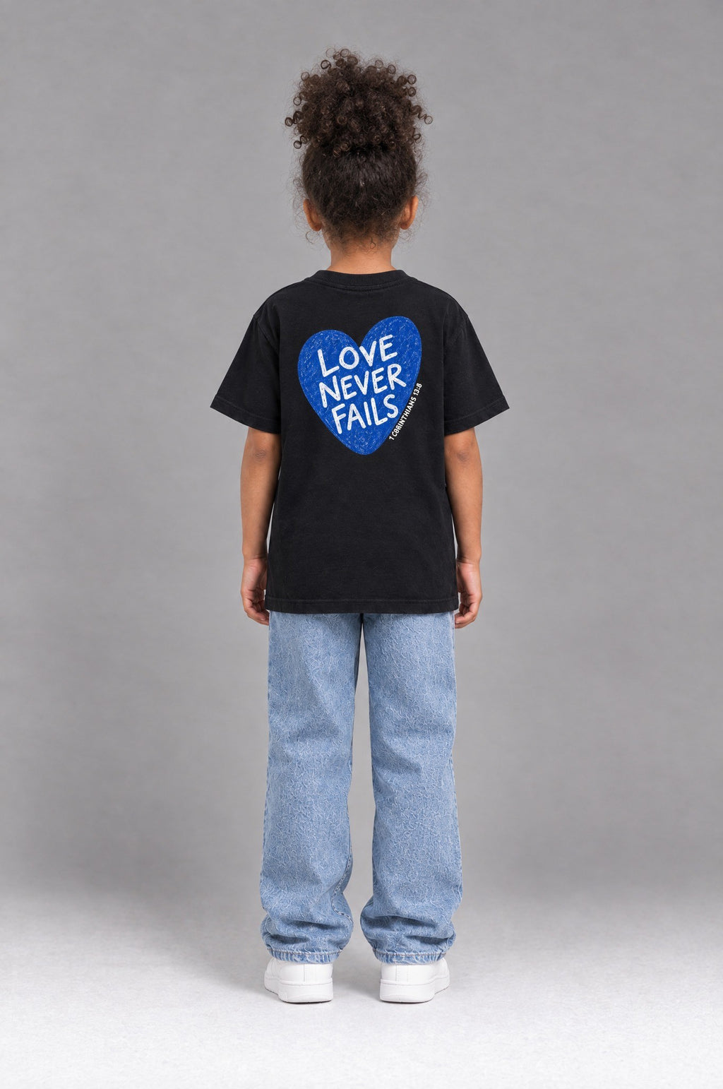 Kind trägt das schwarze Kinder T-Shirt „Love never fails (Herz)“ von Little Faith