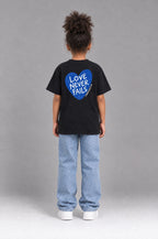 Kind trägt das schwarze Kinder T-Shirt „Love never fails (Herz)“ von Little Faith