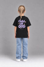 Kind trägt das schwarze Kinder T-Shirt „Child of God“ mit lila Druck von Little Faith