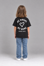 Kind trägt das schwarze Kinder T-Shirt „He knows my name (Heart)“ von Little Faith