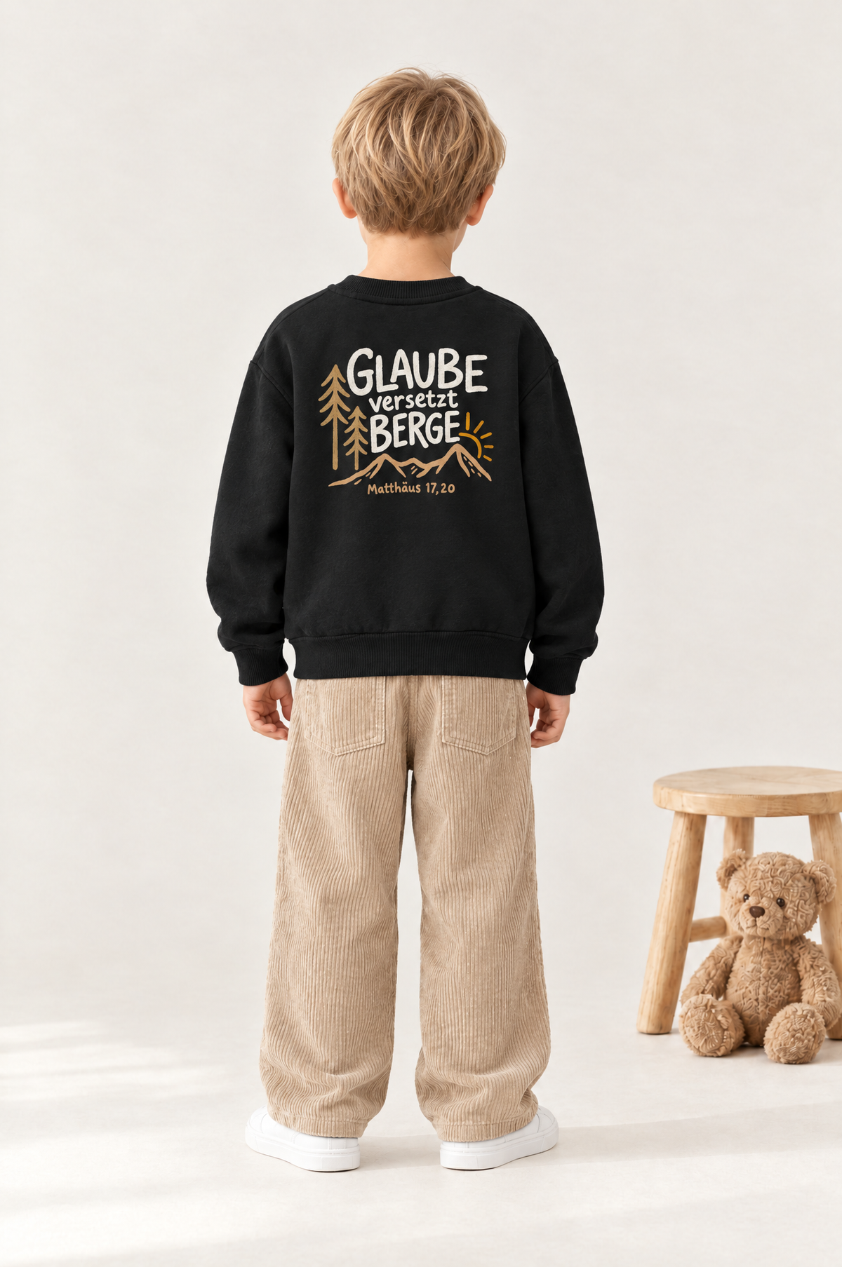 Kind von hinten im Kinder-Sweater „Glaube versetzt Berge“ in Schwarz