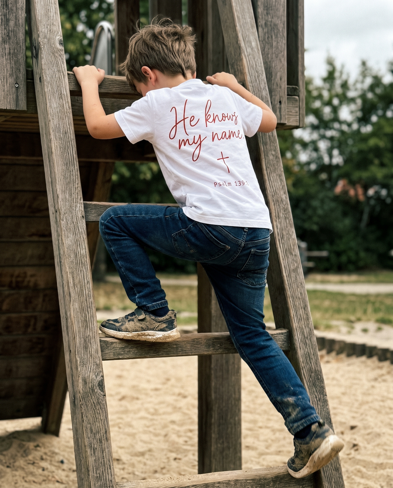 Junge klettert auf dem Spielplatz, weißes T-Shirt mit Rückenprint He knows my name
